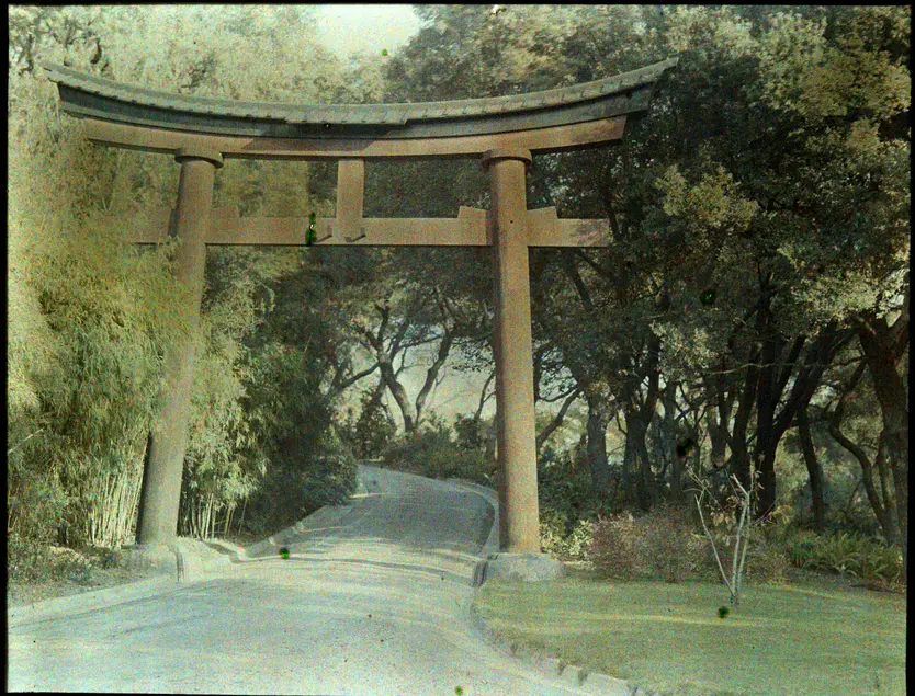 A faded color photograph of a wooden structure frames a path through a garden. The structure has a rectangular form with a bowed upper section.