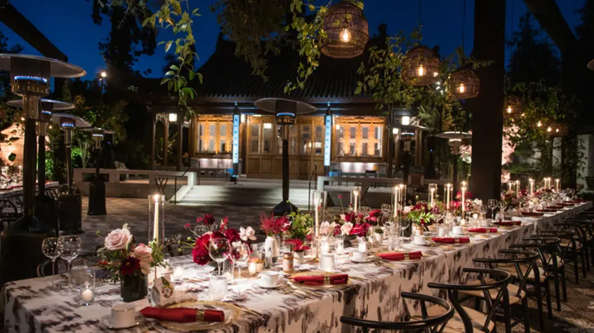 An outdoor courtyard is lit up at night while a long table set up for dinner service awaits guests.