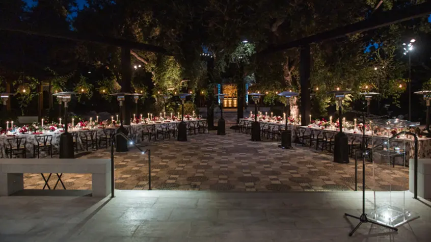 An elevated concrete stage opens up to a courtyard with two long tables set up for dinner service.