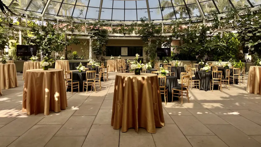Cocktail tables set up with gold tablecloths under a glass dome.