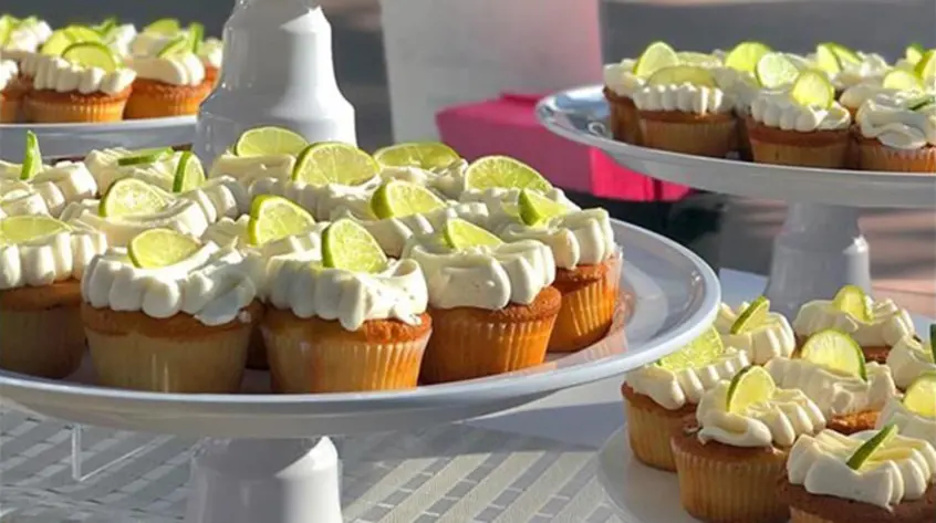 Trays of cupcakes topped with frosting and fresh slices of lime.