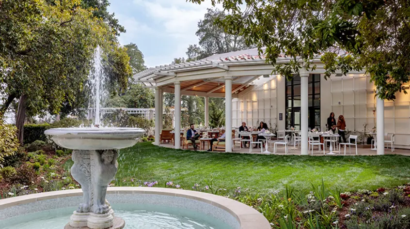 A large garden fountain stands in front of an open pavilion dining area.