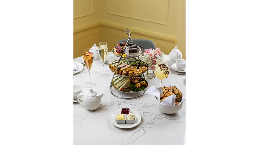 A multi-tiered stand with petite desserts and sandwiches surrounded by champagne, tea, and baked goods..