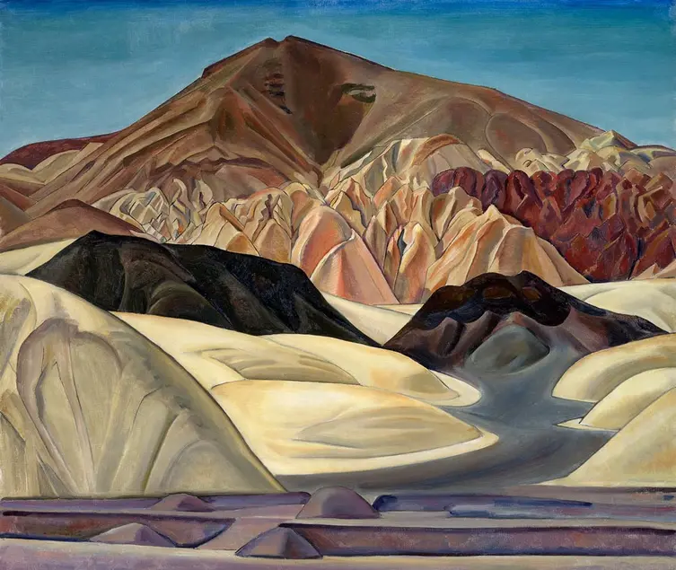 A desert landscape, depicting mountains and sand dunes against a blue sky.