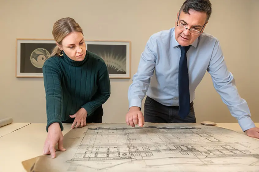 Two people look down at an architectural drawing set on a table.
