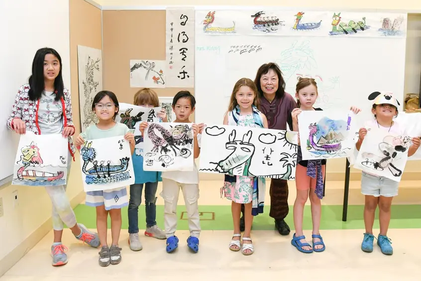 Children stand in a row showing off their painted artworks.