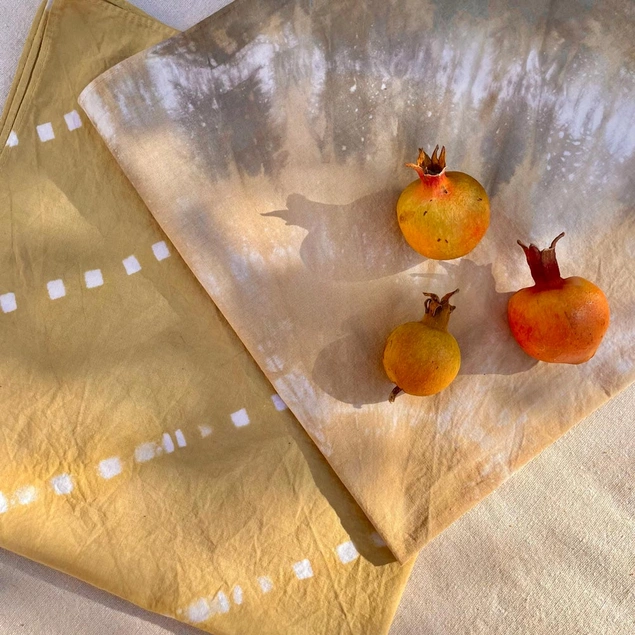 Dyed napkins are folded on a table, with small pomegranates on top.