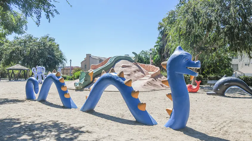 A blue sea serpent play structure in a playground with other sea animal structures.