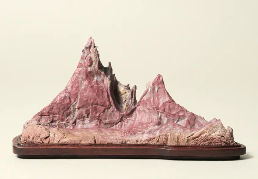 A pink-ish stone, resembling a mountain range, set in a wooden base.