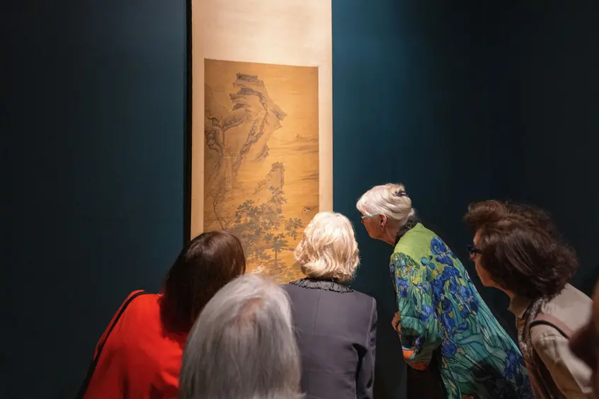 A group of people gathered to look closely at a painting.