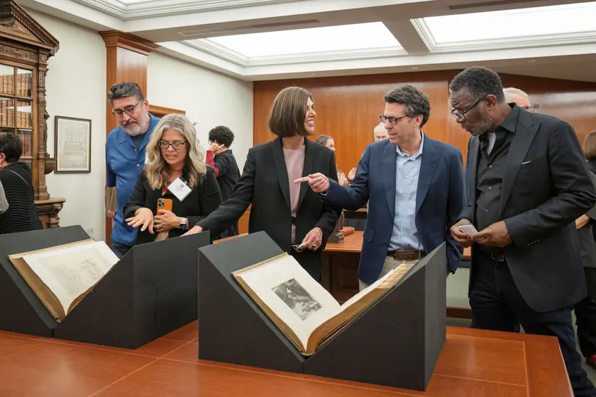 A group of people stand behind a table looking at books.