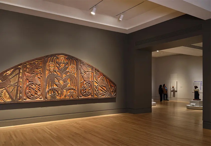 A large carved wood panel on a gallery wall.