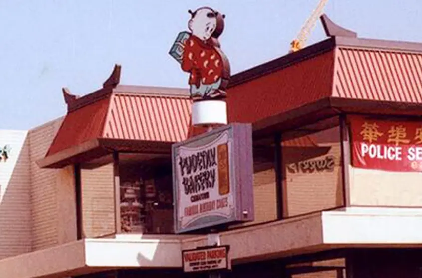 A close-up view of a bakery sign that stands in front of a two-story building.
