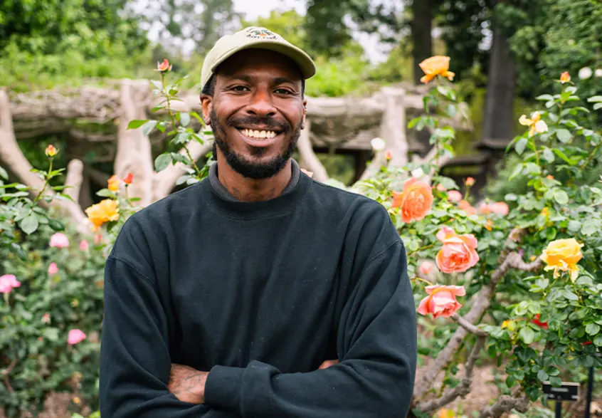 A smiling person stands in a rose garden.