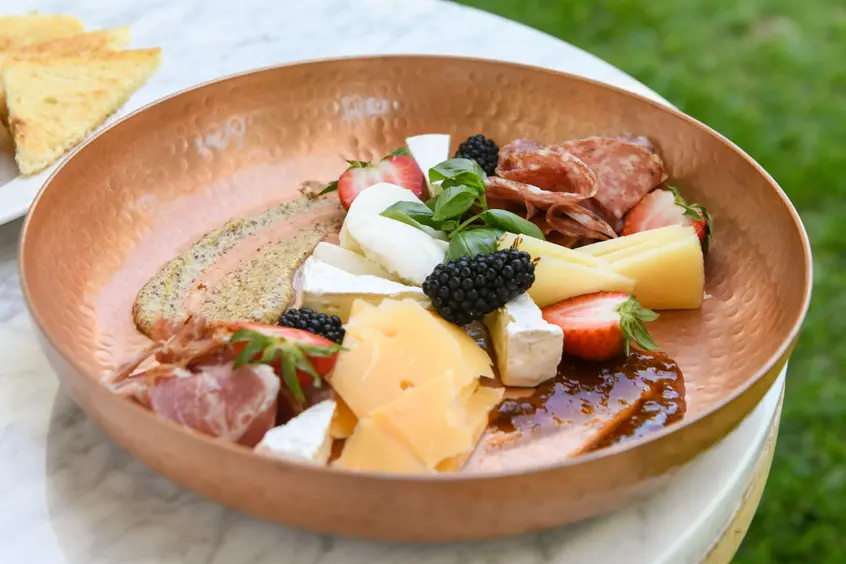 A low metal bowl filled with various sauces, cheeses, fruits, and cured meat.