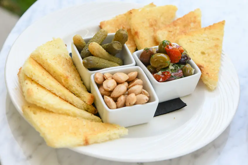 A plate of olives, pickles, nuts, and bread.