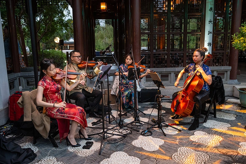 Musicians play stringed instruments in an outdoor courtyard.