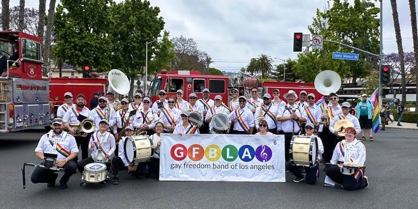  A band poses for a group photo in front of a fire truck, holding a sign that reads “GFBLA Gay Freedom Band of Los Angeles.”