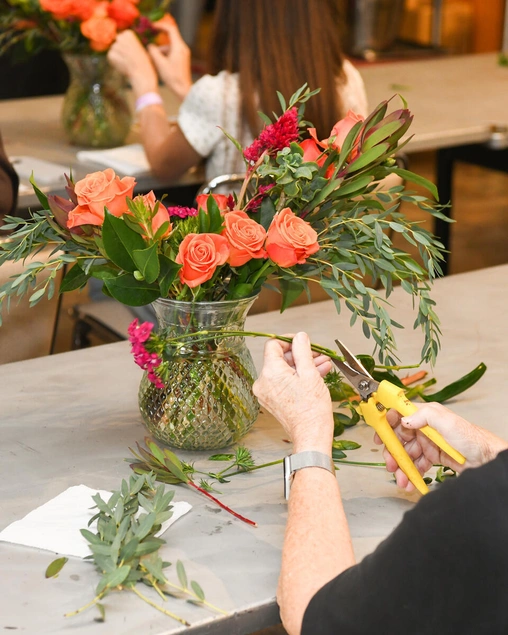 A person trims green foliage in a vase of peach roses.