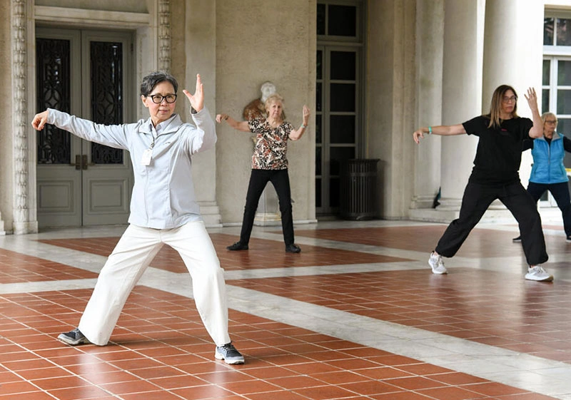 Kathy Chyan leads people in a tai chi pose on a loggia.