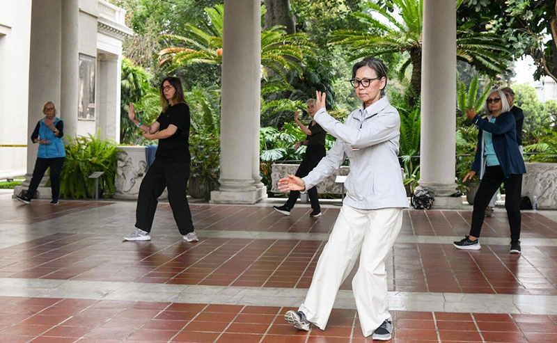 Kathy Chyan leads people in a tai chi pose on a loggia.