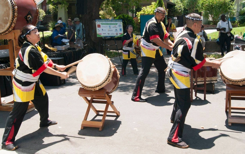 A group of people perform with drums in an outdoor courtyard.