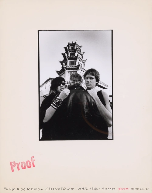 A grayscale image of three people standing in front of an ornate tower, the center person faces away from the camera while the people on the outside face forward, the image is centered on a large beige page with a red "Proof" stamp, and handwritten text along the bottom edge reading "PUNK ROCKERS - CHINATOWN - MAR. 1980 - GUSMANO - © 1980 - MADAM WONG."