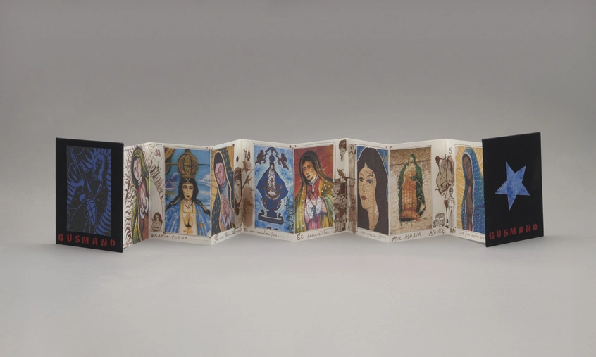 An accordion style book with black front and back cover with blue imagery and red text "GUSMANO," the interior includes eight pages filled with colorful religious imagery, sepia-tone illustrations, and handwritten text along the bottom.