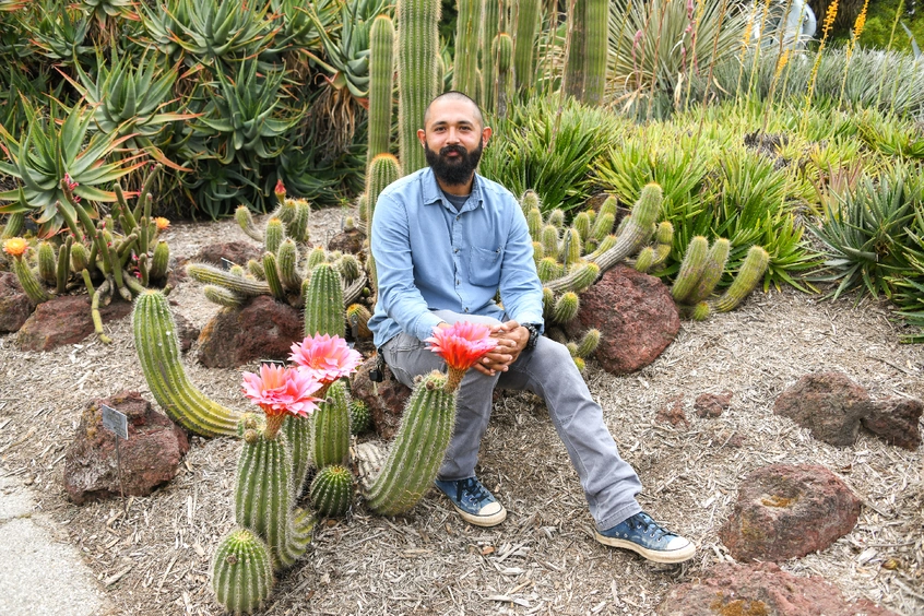 A person in a blue shirt sits in a desert garden.