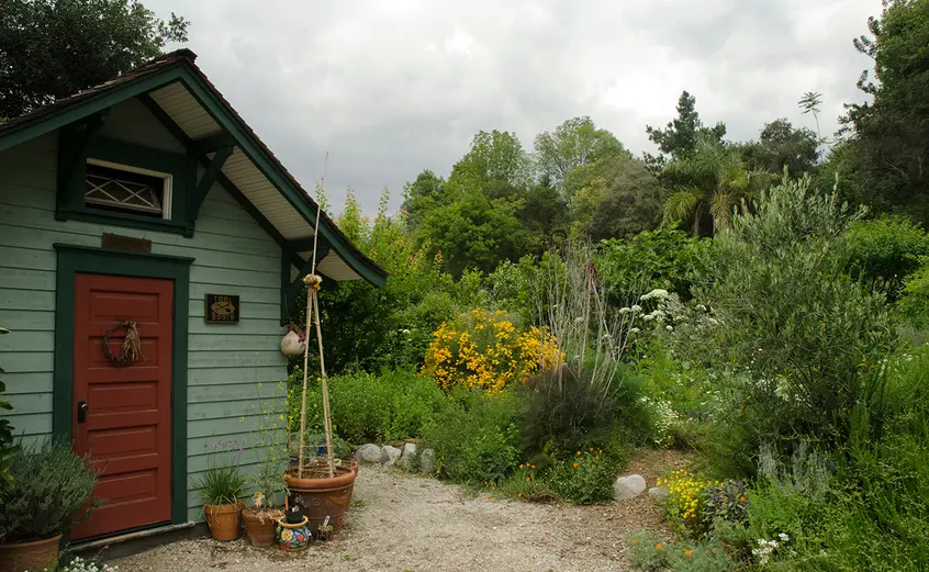 Several flowers surround the green Ranch Garden shed