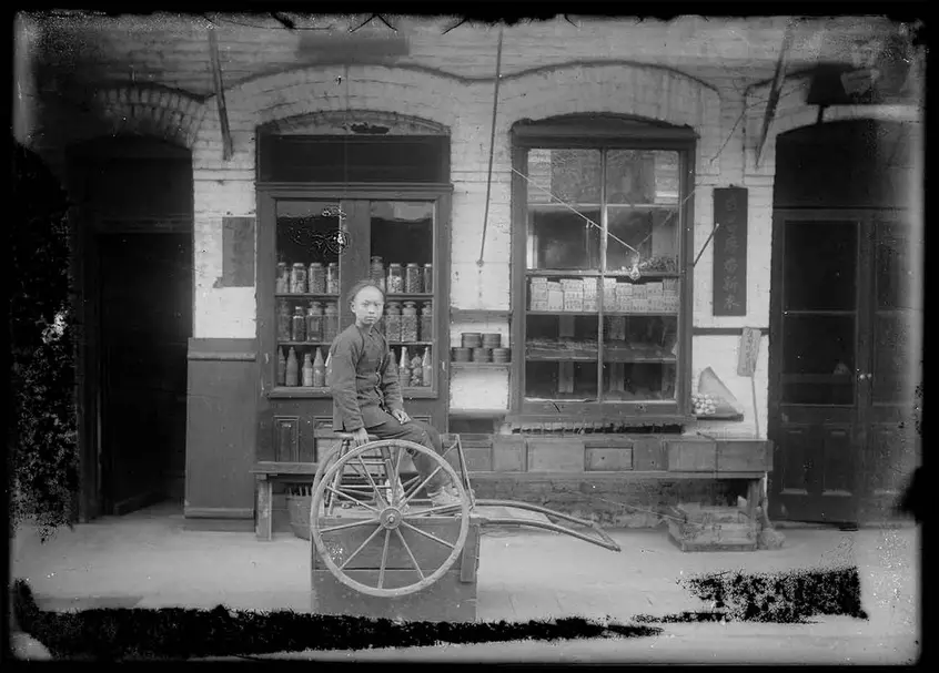 Unknown photographer, Young store clerk sitting in front of shops selling poultry and clothing, Old Chinatown, Los Angeles, ca. 1900. The Huntington Library, Art Museum, and Botanical Gardens.