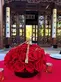 A bouquet of deep red roses accents a red tablecloth covered table in front of a Chinese-designed glass building.