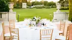 A round event table with light wood chairs looks out onto a large grassy area.