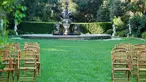 Wooden chairs set up on a green lawn with a large garden fountain in the background.