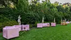 Pink velvet couches and chairs set up along a grassy garden.