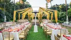 Strips of yellow fabric hang over tables on a grassy lawn.