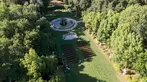 Overhead view of a lawn surrounded by lush trees. A large fountain and small wedding event set up sit in the middle of the lawn.