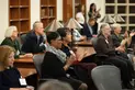 A group of people sit in a library, clapping and smiling.