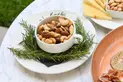 A bowl of nuts on a plate with rosemary sprigs.