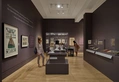 Two people look at objects in museum gallery display cases.