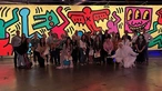 A group of people pose in front of a brightly lit and colorful artwork by Keith Haring.