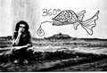 Grayscale image of a person squating on a dirt patch in front of a white wall with graffiti of a stylized fish and 