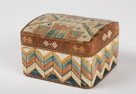 Angled view of a small colorful box with a lid, decorated with lengths of porcupine quills forming a geometric design on the lid and chevron patterns on sides.