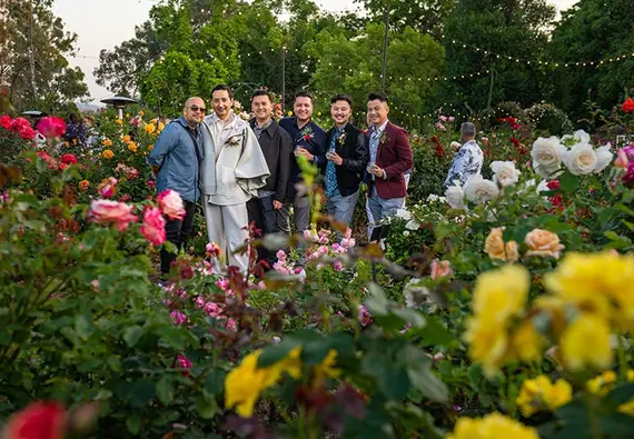 A group of six people pose for the camera surrounded by blooming roses.