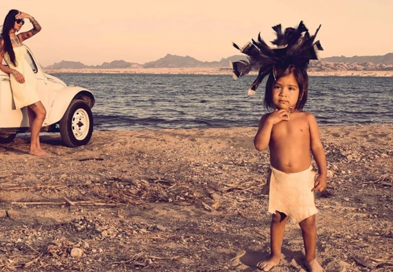 A book cover with a photo of a child on sandy ground near a body of water, text reads "We Are the Land, A History of Native California"