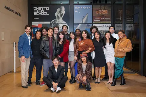 A group of 17 people standing in front of a museum gallery display.
