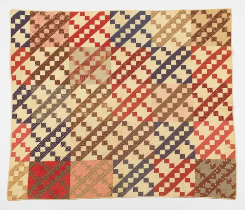 Quilt with Jacobs Ladder pattern in shades of tan, red, and blue.