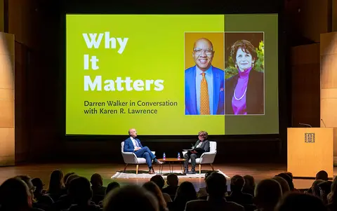 An audience watches two people conversing on a stage with a large graphic behind them that says "Why It Matters."