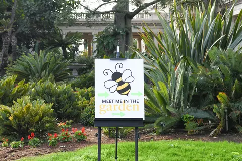 A sign in a garden, reading "Meet Me in the Garden/"