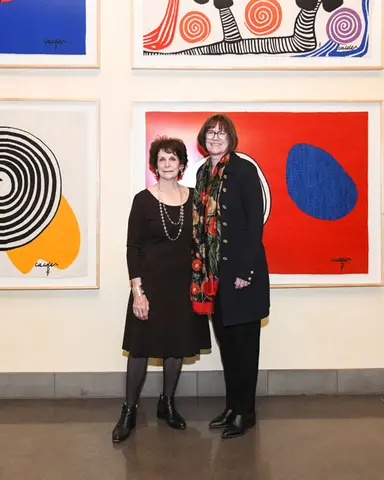 Two people stand together in front of a wall of framed artwork.